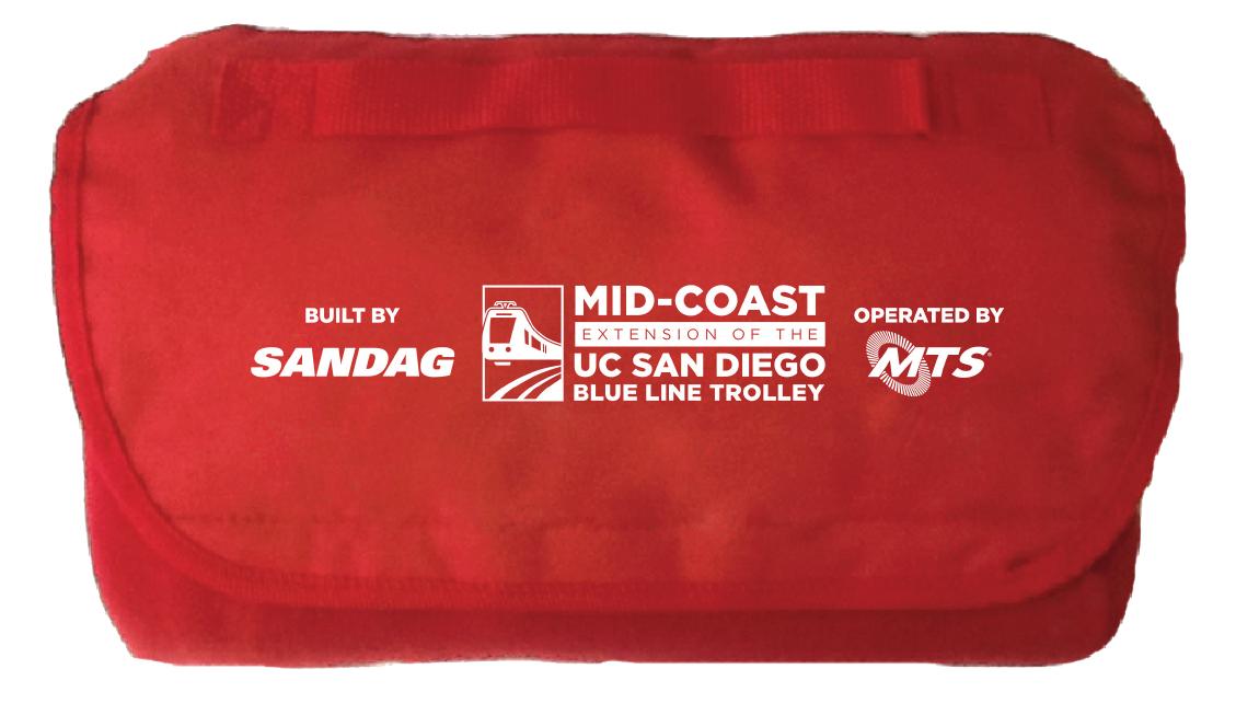 Red fleece blanket featuring Mid-Coast Trolley project logo, SANDAG logo, and MTS logo